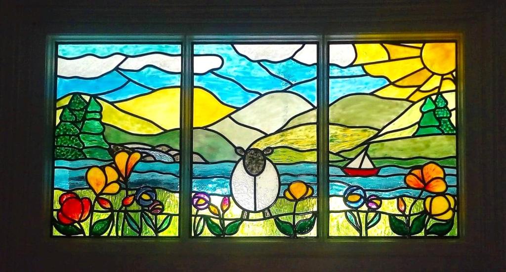 Stained glass window with sheep, flower and sailing boat motifs